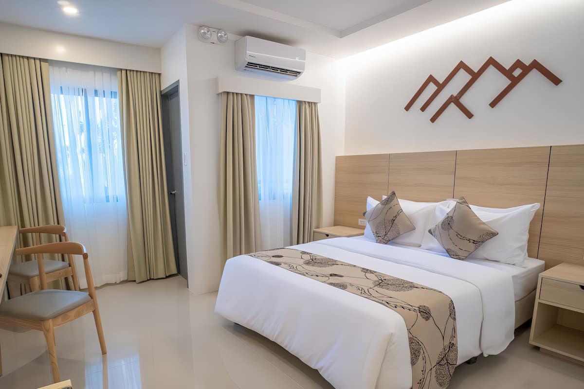 Una habitación de hotel con una cama grande, una mesita de noche de madera, un escritorio y una silla.