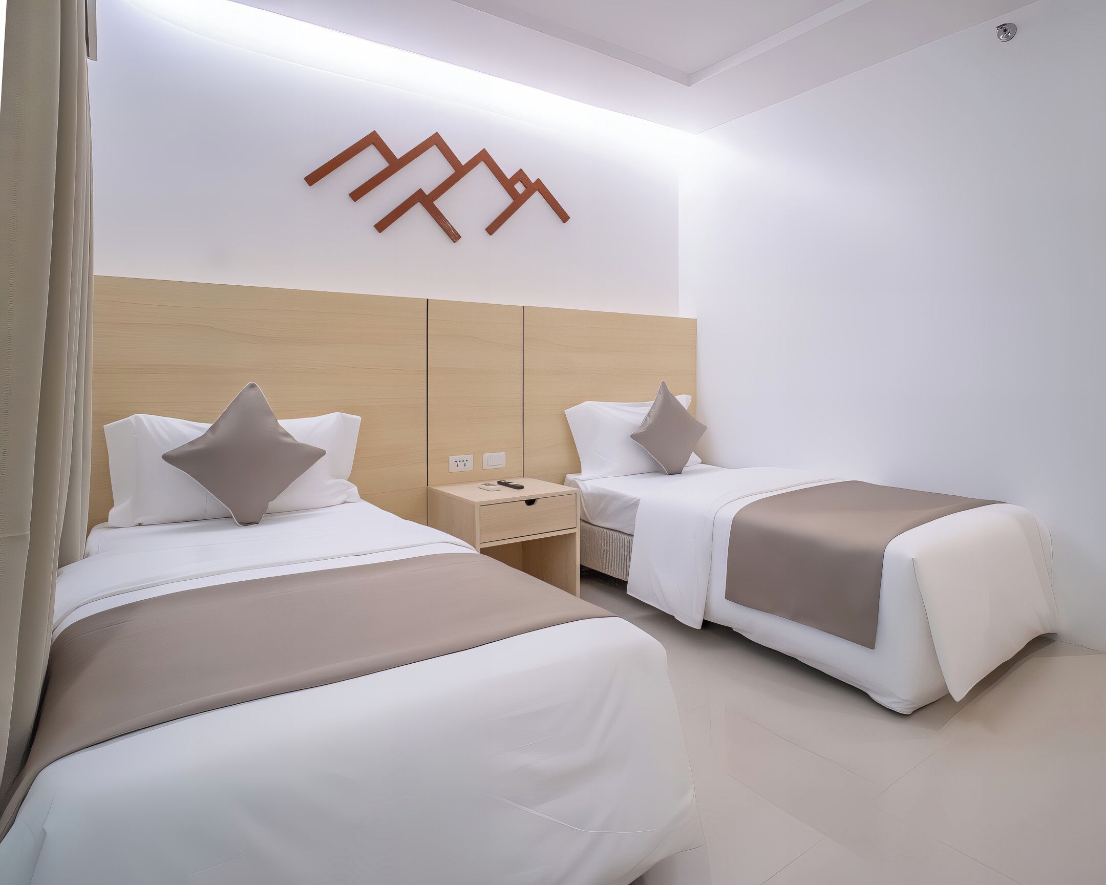 A hotel room with two beds, each with a pillow and a bedside table.