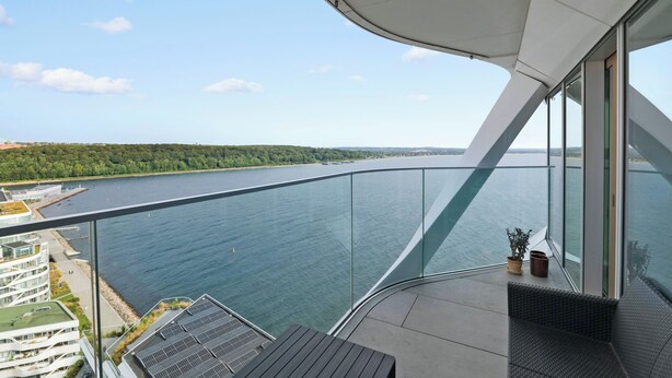 Un balcon doté d’une balustrade en verre, offrant une vue sur une étendue d’eau et une côte lointaine.