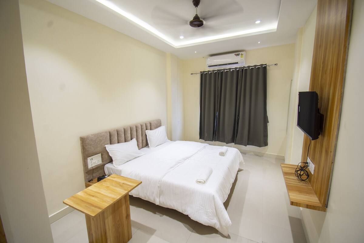 Une chambre moderne avec un grand lit, des tables de chevet, un ventilateur de plafond, un appareil de climatisation et un téléviseur fixé au mur.