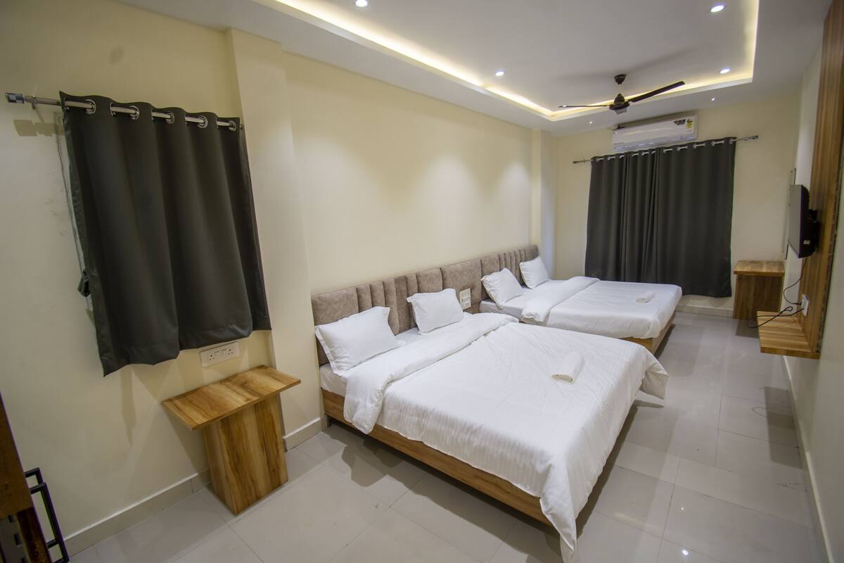 Une chambre d’hôtel avec trois lits, un ventilateur de plafond et une télévision.