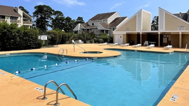 A swimming pool with a lifeguard tower, lounge chairs, and a building with a sign indicating no lifeguard on duty. - LR2 Bay Tree great studio + pool in Little River (Little River)