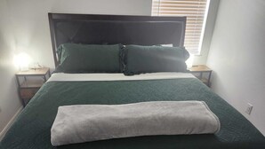 Una cama con un edredón verde oscuro, dos almohadas, una manta blanca y una toalla blanca encima.