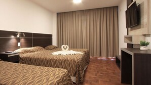 A hotel room with a large bed, a smaller bed, a desk, a TV, and a plant. - Hotel Grand Prix (Villa Carlos Paz)