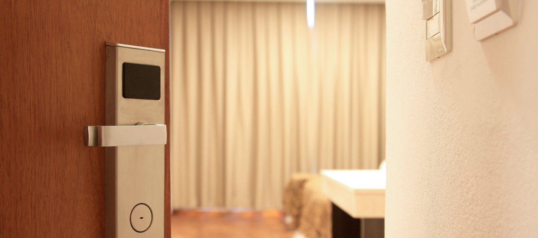 A modern door with a card reader, a wall-mounted light switch, and a wooden floor.