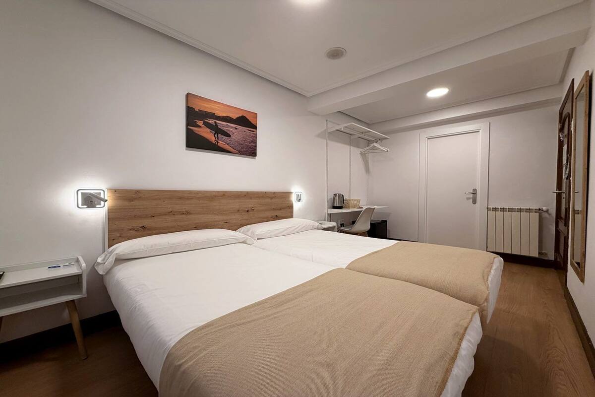 Une chambre d’hôtel avec deux lits, une tête de lit en bois, des tables de chevet, un bureau et une chaise.