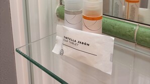 A glass shelf with a soap tablet packet labeled "PASTILLA JABÓN SOAP TABLET" and two bottles of soap. - PENSIÓN SANTA CLARA SAN SEBASTIAN (San Sebastián)