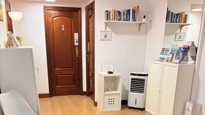 A room with a wooden floor, white chairs, a small table, a bookshelf, a white cabinet, and a door with a number. - PENSIÓN SANTA CLARA SAN SEBASTIAN (San Sebastián)