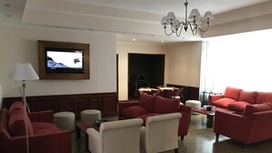 Une chambre d’hôtel avec un canapé rouge, un téléviseur à écran plat fixé au mur, un coin repas comprenant une table et des chaises, et un lustre.