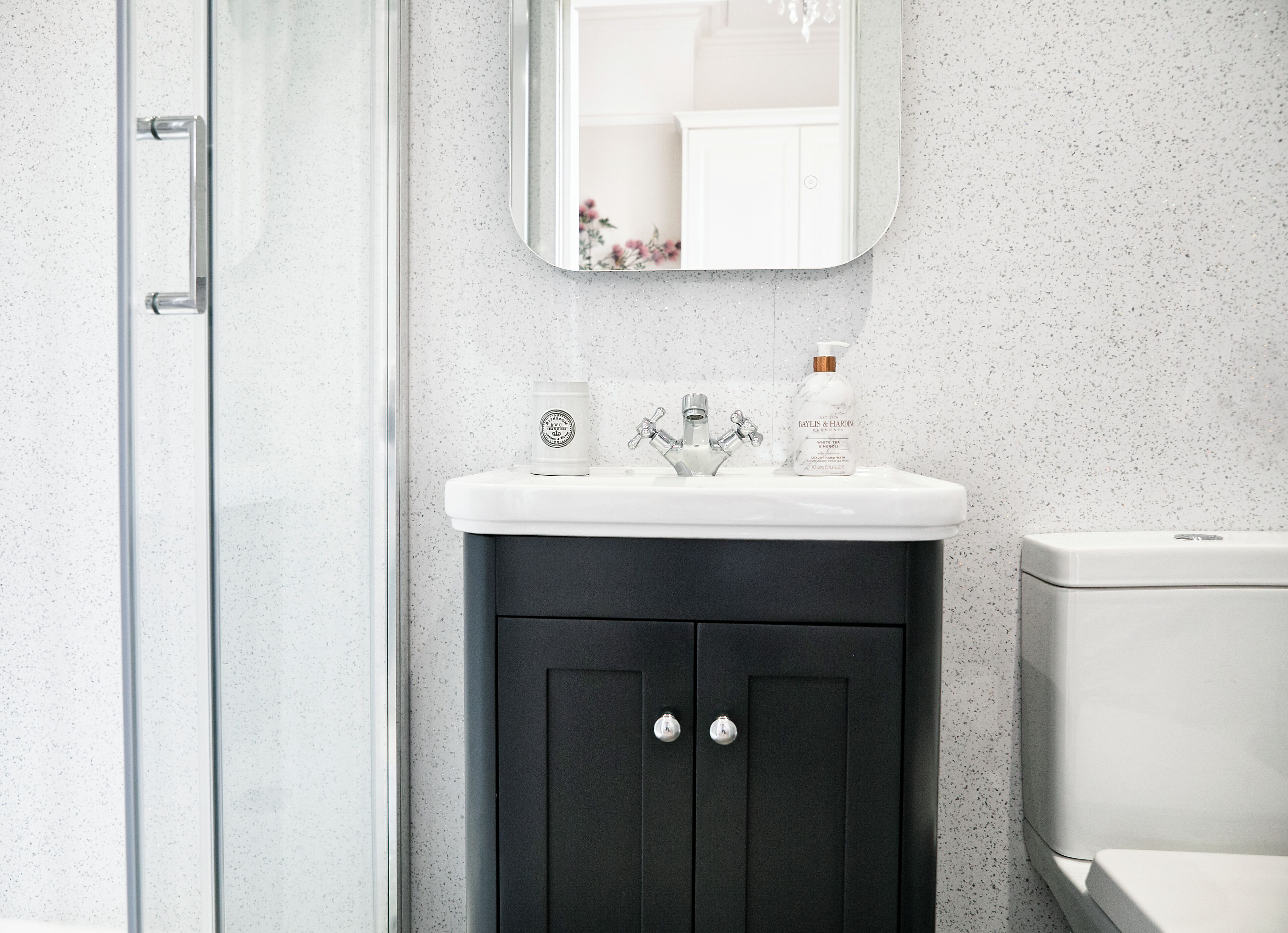 A modern bathroom with a glass shower enclosure, a white sink with a marble countertop, a black cabinet with silver handles, and a white toilet.