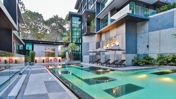 A modern hotel with a swimming pool, lounge chairs, and a glass railing.