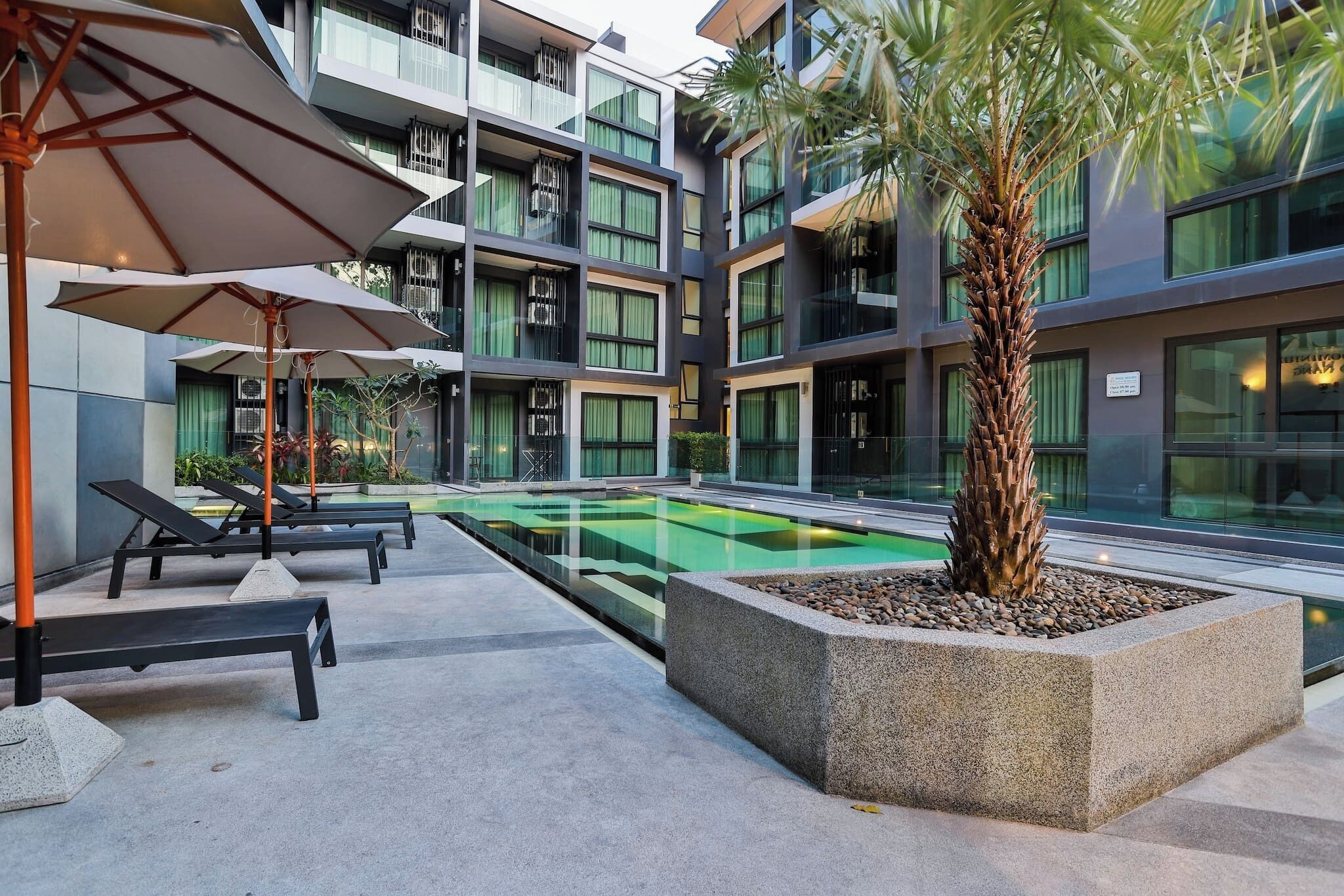 Un bâtiment moderne doté de nombreux balcons, d’une piscine, de chaises longues et de parasols.