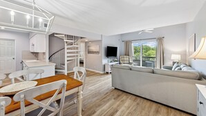 A modern living room with a sofa, dining table, and chairs. There is a staircase leading to an upper level. - 891 Ketch Court @ Harbour Town, Sea Pines | Walk to Marina & Golf Links | Pet-Friendly! (Hilton Head Island)
