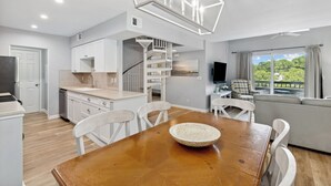 A modern kitchen with white cabinets, a wooden dining table, and a large window with a view of greenery. - 891 Ketch Court @ Harbour Town, Sea Pines | Walk to Marina & Golf Links | Pet-Friendly! (Hilton Head Island)