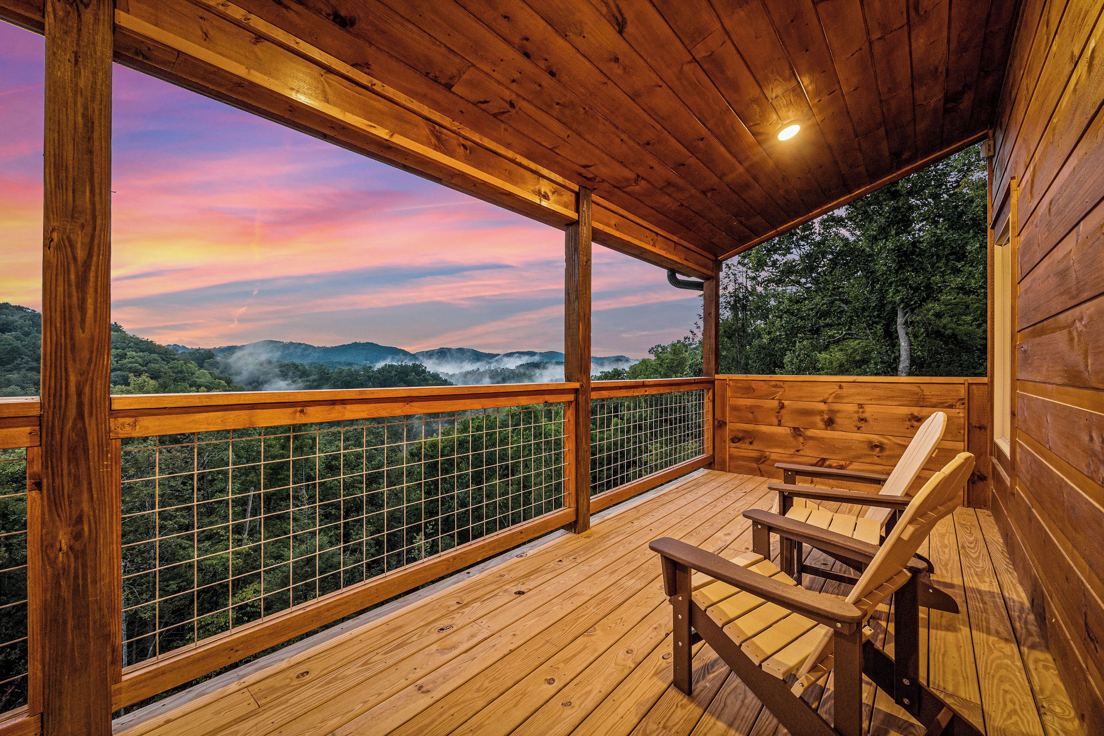 A wooden deck with a view of a forested mountain range and a sunset.