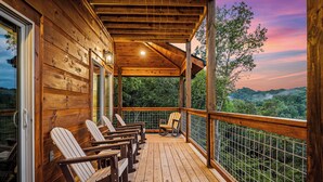 Um deck de madeira com cadeiras de balanço e uma porta de vidro que dá para uma varanda com vista para a floresta.