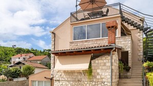 A two-story house with a stone facade, a balcony with outdoor furniture, and a staircase leading to the upper floor. - Apartment Nature View near Dubrovnik (Zupa dubrovacka)