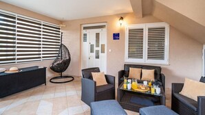 A modern lounge area with a black hanging chair, wicker sofas, and a glass table set with breakfast items. - Apartment Nature View near Dubrovnik (Zupa dubrovacka)