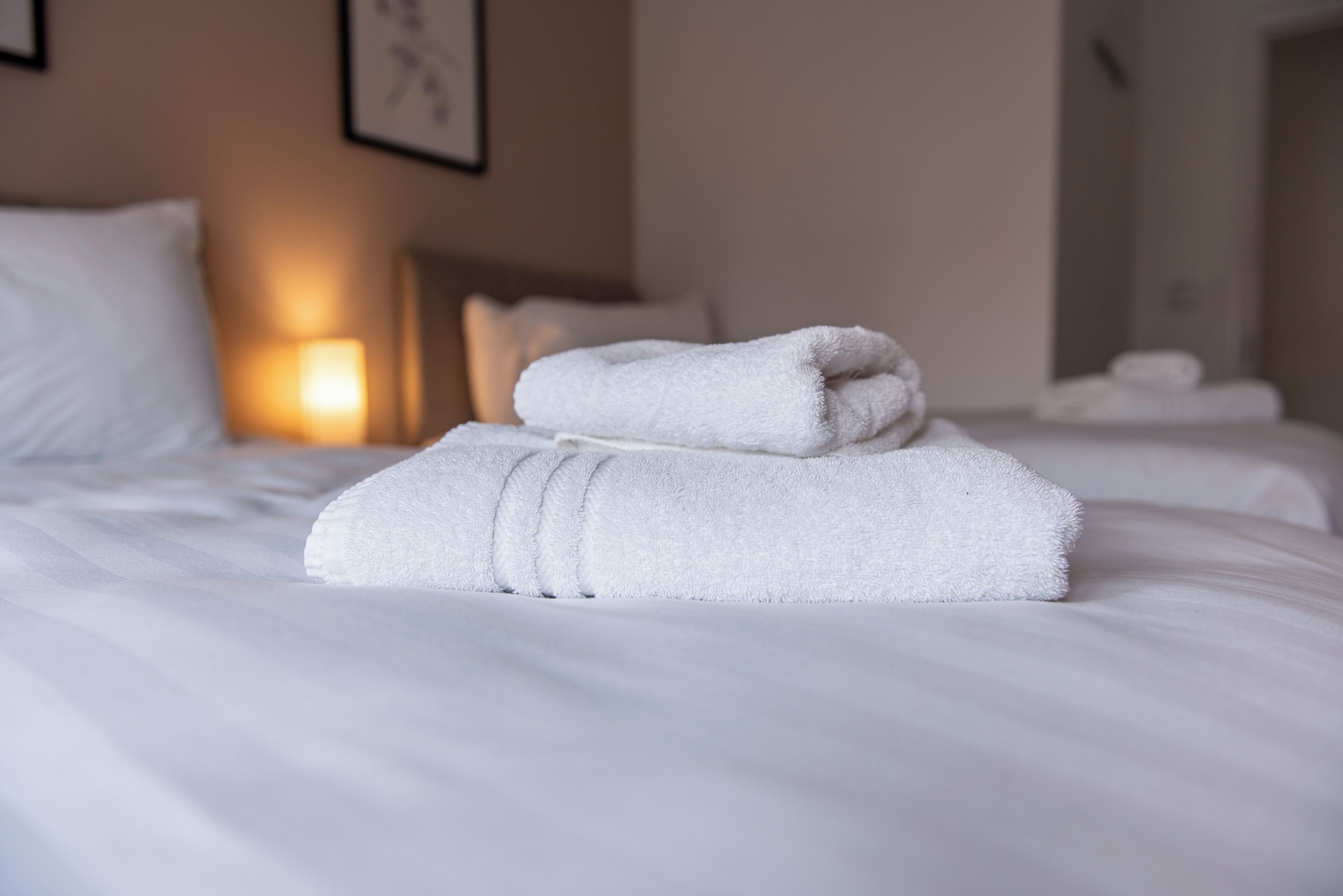 A neatly made bed with white linens and a folded towel on top.
