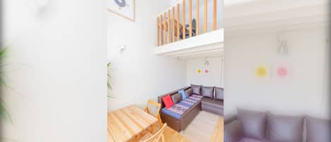 A modern living space with a wooden dining table, a sofa with patterned cushions, and a staircase leading to an upper level.