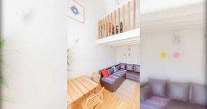 A modern living space with a wooden dining table, a sofa with patterned cushions, and a staircase leading to an upper level. - Delightful 3BD Family Home w Garden, Finsbury Park (Greater London)