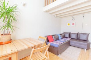 En stue med et træspisebord, en grå sofa med puder og en potteplante.