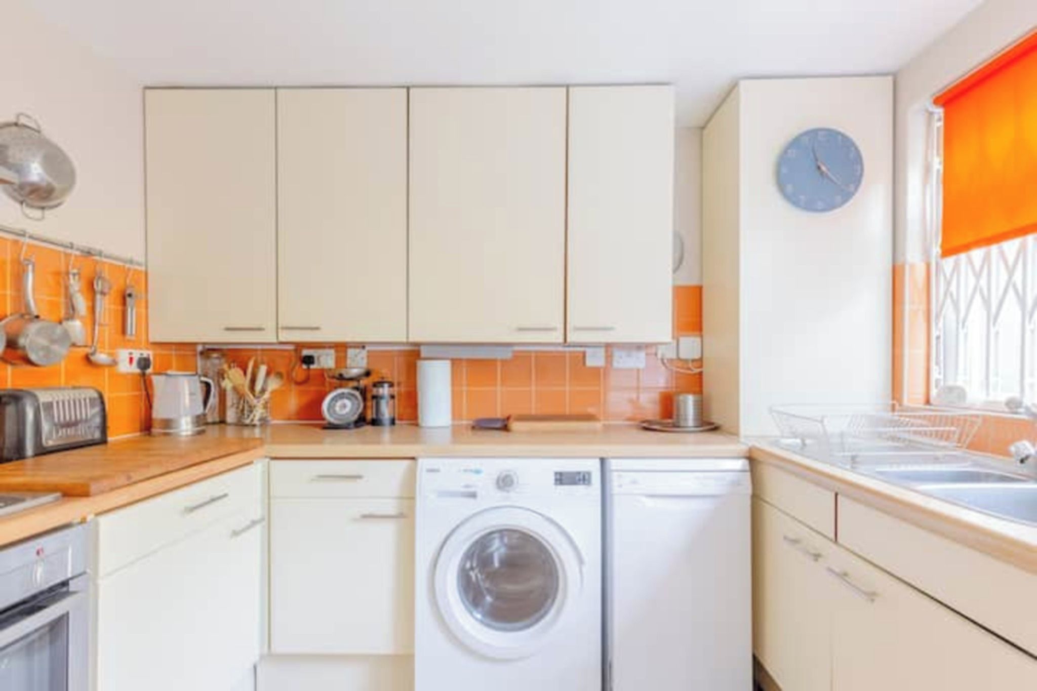 Cocina compacta con lavadora, tostadora y un reloj en la pared.