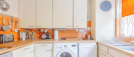 A compact kitchen with a washing machine, a toaster, and a clock on the wall.
