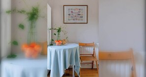 Un comedor con una mesa redonda, sillas, un jarrón con flores y un cuadro en la pared.