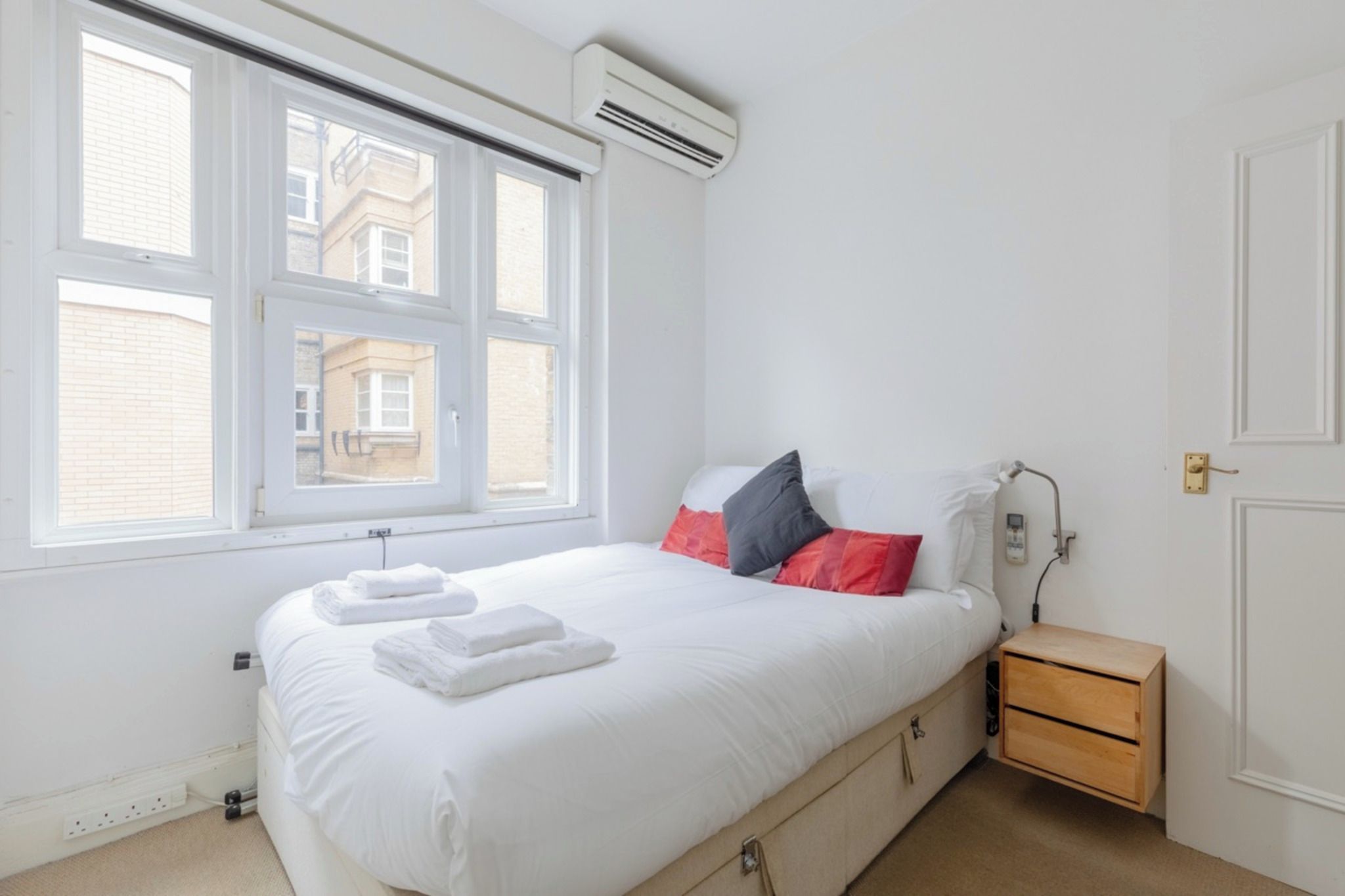 Een slaapkamer met een bed, een raam, een airconditioning en nachtkastjes.