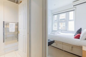 A hotel room with a bed, a window with blinds, a radiator, and a towel rack.