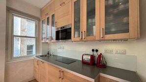 A modern kitchen with wooden cabinets, a built-in microwave, and a toaster. - Superbly Located 1BD Flat, Heart of Fitzrovia (Greater London)