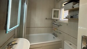A bathroom with a bathtub, a sink, a mirror, and a window. - Superbly Located 1BD Flat, Heart of Fitzrovia (Greater London)