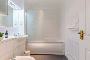 A modern bathroom with a bathtub, a sink, a mirror, and a toilet.