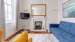 A living room with a fireplace, a blue sofa, a yellow armchair, and a TV. - Stylish 1BR Flat by Museums in South Kensington (Greater London)