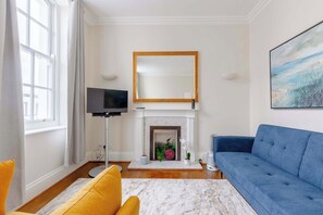Un salon avec une cheminée, un canapé bleu, un fauteuil jaune et un téléviseur.