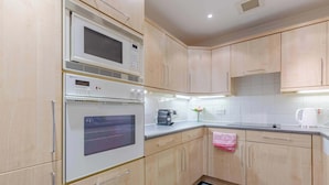 A kitchen with wooden cabinets, a microwave, an oven, a coffee maker, and a tiled backsplash. - Stylish 1BR Flat by Museums in South Kensington (Greater London)