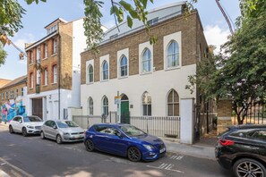 A street view with a row of parked cars, a building with arched windows, and a mural on the adjacent wall. - One of a Kind 2BDR Flat in Shoreditch (London)