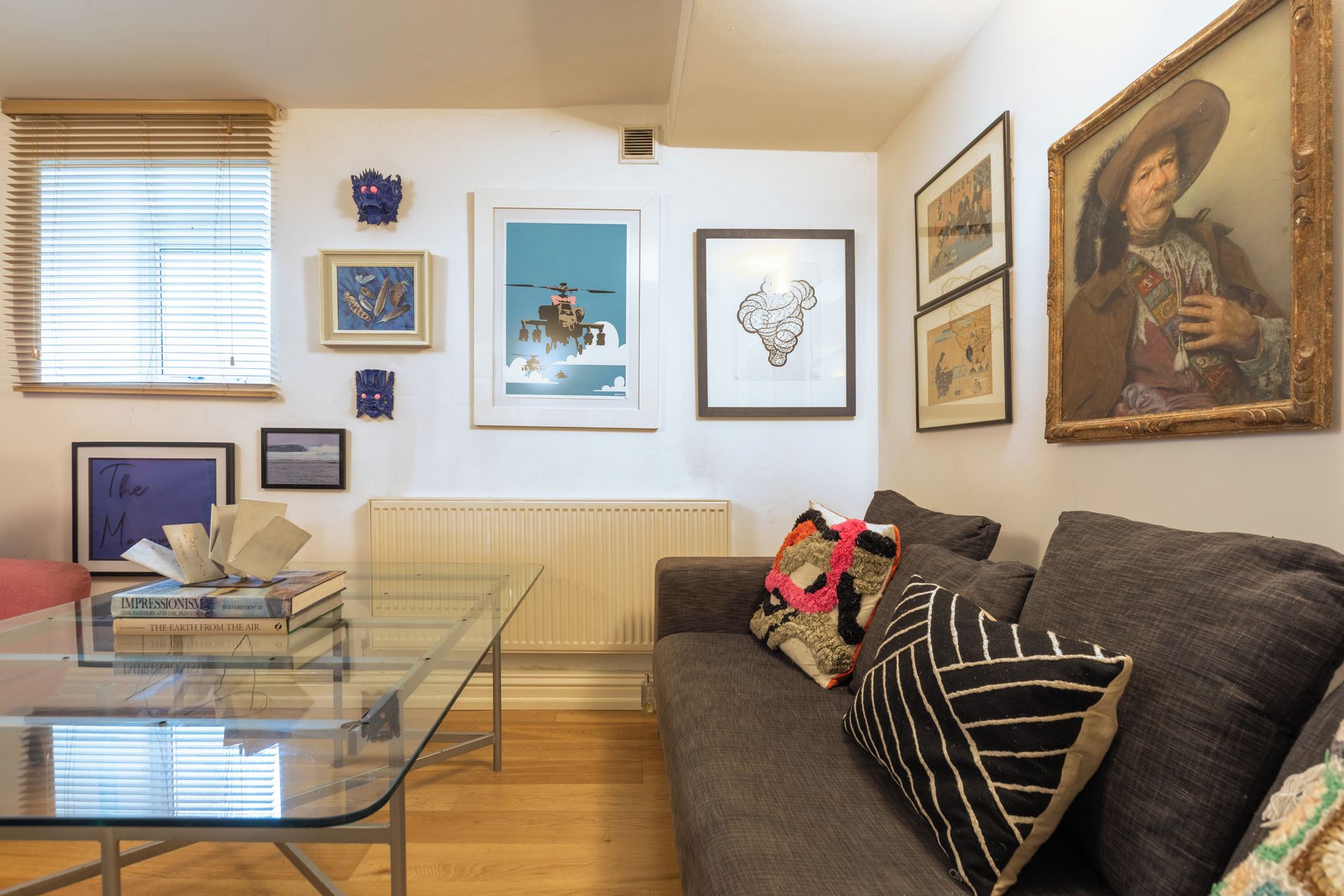 A living room with a glass coffee table, a sofa with decorative pillows, and various framed artworks on the walls.