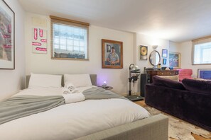 A hotel room with a bed, a desk, a chair, and a sofa. There are pictures on the walls and a window with blinds. - One of a Kind 2BDR Flat in Shoreditch (London)