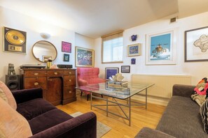 A living room with a glass coffee table, a red armchair, a brown sofa, and a wooden cabinet with a record player. - One of a Kind 2BDR Flat in Shoreditch (London)