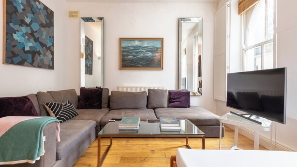 Un salon moderne avec un canapé d’angle, une table basse en verre, un téléviseur à écran plat et des œuvres d’art accrochées aux murs.
