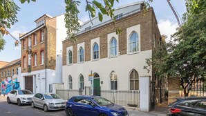 A street view with a row of parked cars, a building with arched windows, and a mural on the adjacent wall. - One of a Kind 2BDR Flat in Shoreditch (London)