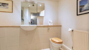 Une salle de bain avec un lavabo blanc, des toilettes en bois, un miroir et un tableau encadré au mur.