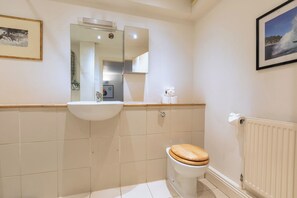 A bathroom with a white sink, a wooden toilet, a mirror, and a framed picture on the wall. - One of a Kind 2BDR Flat in Shoreditch (London)