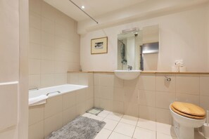 A bathroom with a bathtub, sink, mirror, toilet, and a small rug.