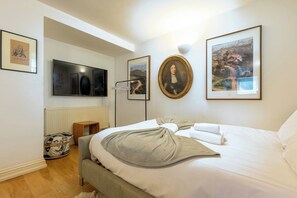 A bedroom with a bed, a television, a framed portrait, and a radiator.