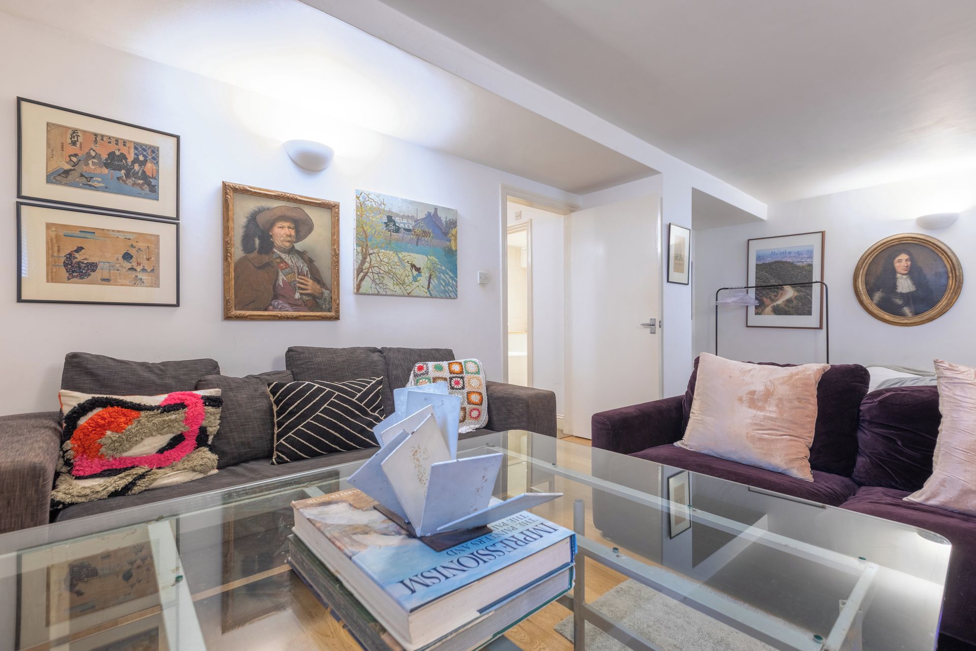 Un salon avec une table basse en verre, deux canapés et divers tableaux encadrés accrochés aux murs.