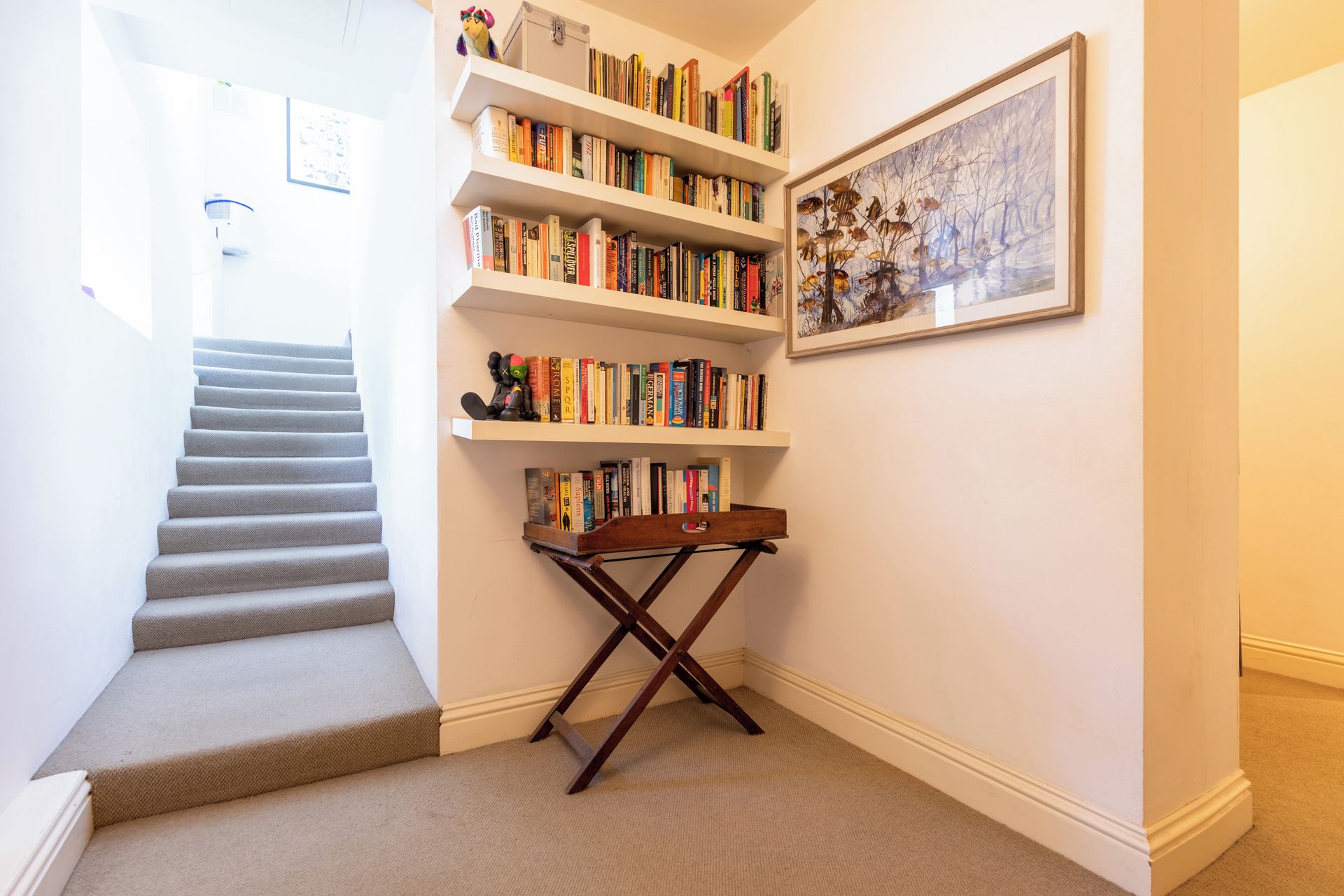 Eine Treppe führt zu einer Zwischenebene mit einem Bücherregal und einem gerahmten Bild an der Wand.