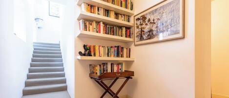 Eine Treppe führt zu einer Zwischenebene mit einem Bücherregal und einem gerahmten Bild an der Wand.